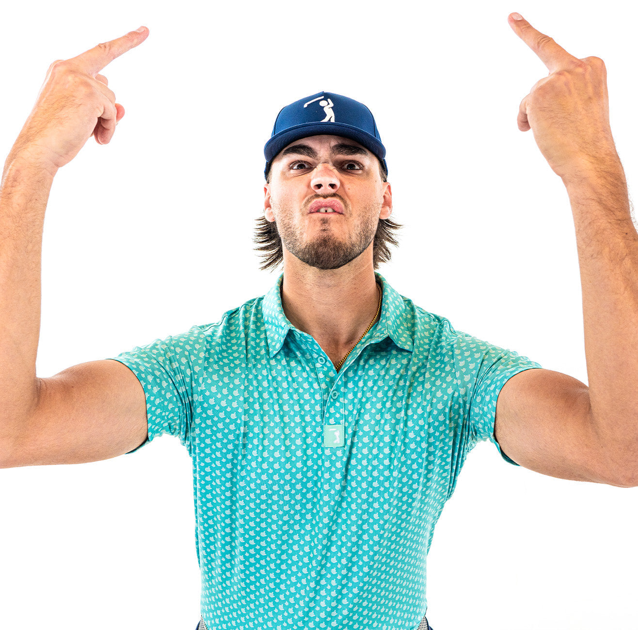 A man in a teal patterned polo and blue cap makes an angry face while raising both hands and extending his middle fingers upward against a plain white background.