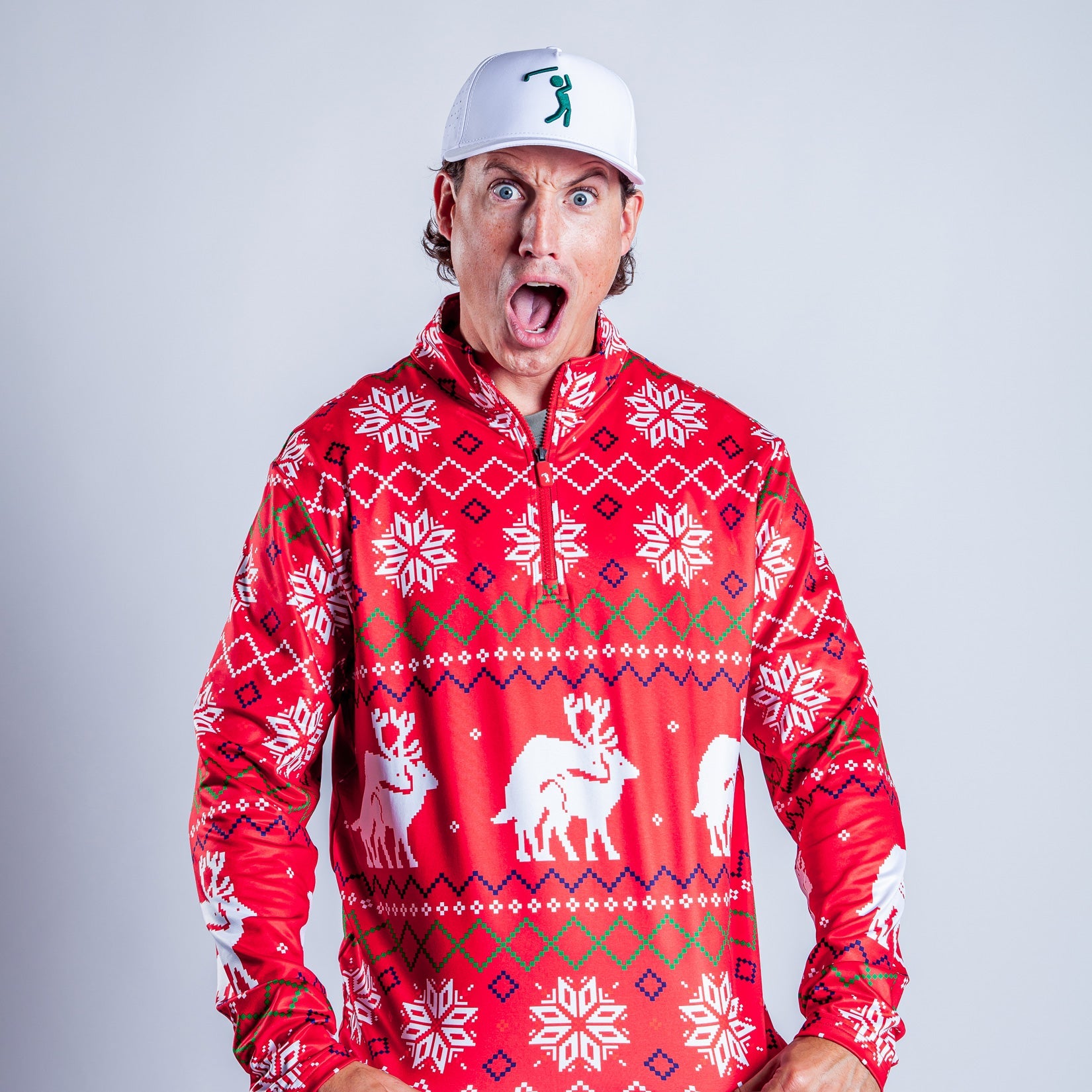 A surprised man in a white cap and festive red sweater with white reindeer and snowflake patterns stands against a plain light background, mouth open in shock.