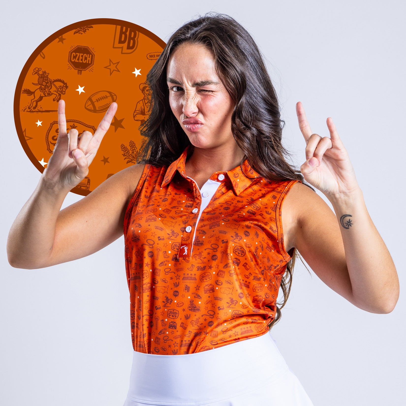 A woman with long brown hair winks and makes rock on hand signs. She wears an orange sleeveless polo with white skirt. A circle highlights her shirt’s pattern—football, cartoon figures, stars, and the word CZECH on a rust-colored background.