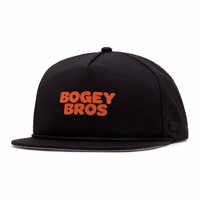 The Wingin' It - Unstructured Flat Bill Hat is a black snapback with bold orange "BOGEY BROS" on the front, made from performance material. Features include side ventilation holes, an adjustable fit, and a sleek black tag near the brim.