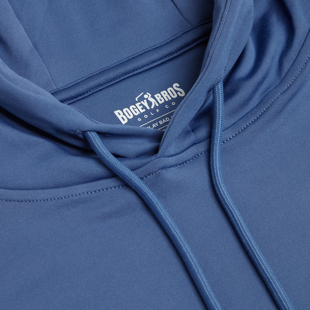 Close-up of the Cooler Blue - Hoodie showing the chest area and hood drawstrings. The inside label reads Bogey Bros Golf Co. and Laybad. The fabric appears smooth and soft, featuring neat stitching, relaxed folds, and a super stretchy feel for added comfort.
