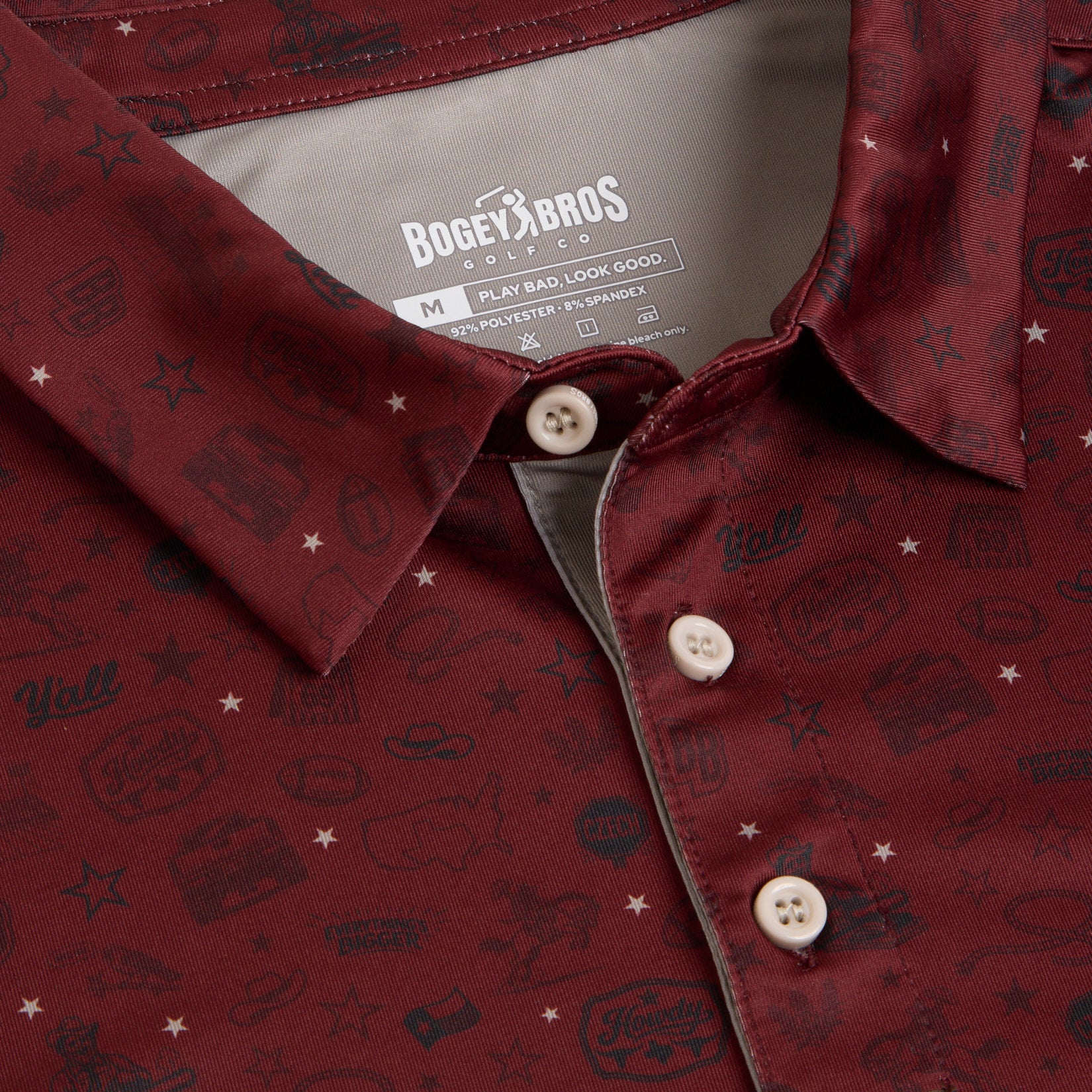 Close-up of a maroon collared shirt with off-white buttons. The fabric features a subtle, playful black pattern of various icons and words. The label inside reads Bogey Bros with shirt details in white text on a gray background.