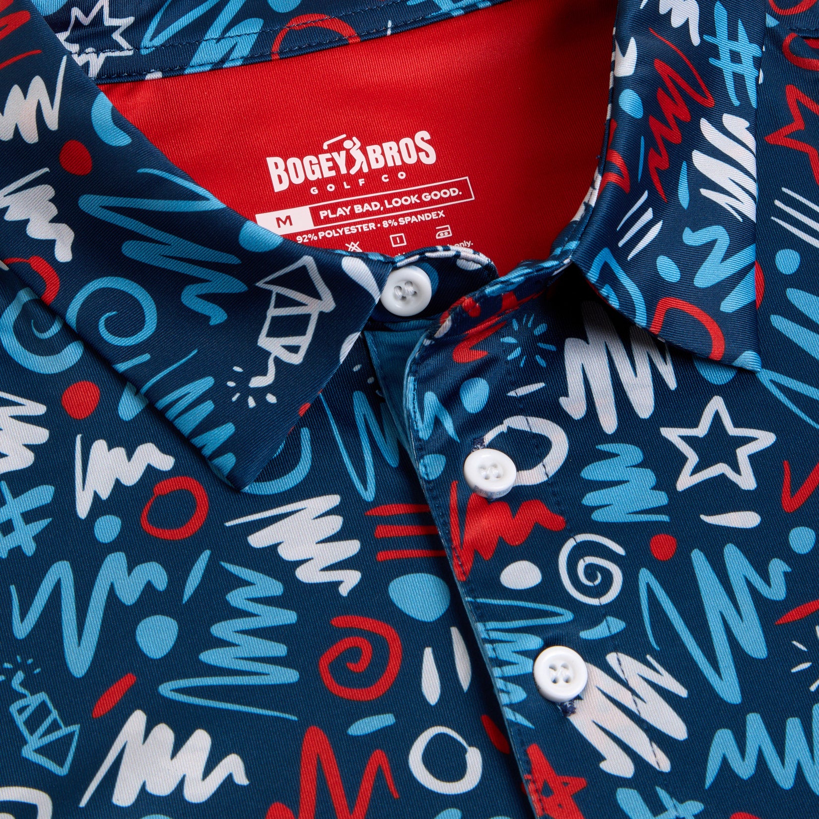 Close-up of a blue collared shirt with white buttons, featuring a bold pattern of white, red, and light blue abstract shapes like zigzags, stars, and swirls. The red inner collar tag reads Bogey Bros along with size and care instructions.