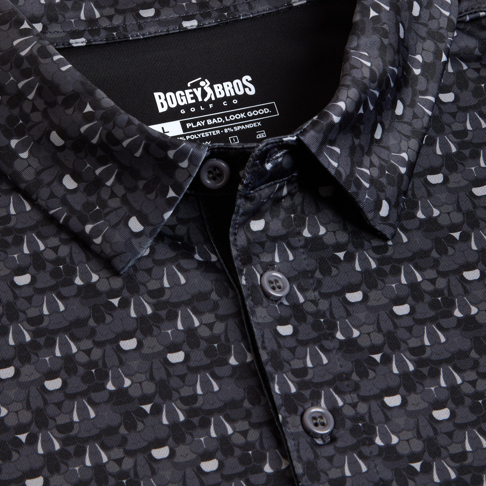 Close-up of the T&A - Fitty Shades - Polo: an athletic fit shirt with a dark gray and black abstract pattern, three buttons, and UPF 50 protection. Inside the collar, the Bogey Bros label reads Play Bad, Look Good above care details.