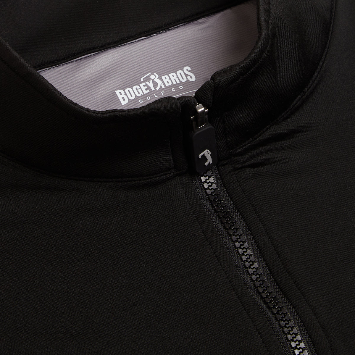 Close-up of the Black - Q-Zip jacket, featuring a black exterior with gray lining. The zipper pull is accented with a golf club design, and the inside collar label displays BOGEY BROS GOLF CO in white letters. Crafted from smooth, slightly stretchy fabric, this jacket offers an athletic fit and moisture-wicking properties for all-day comfort.