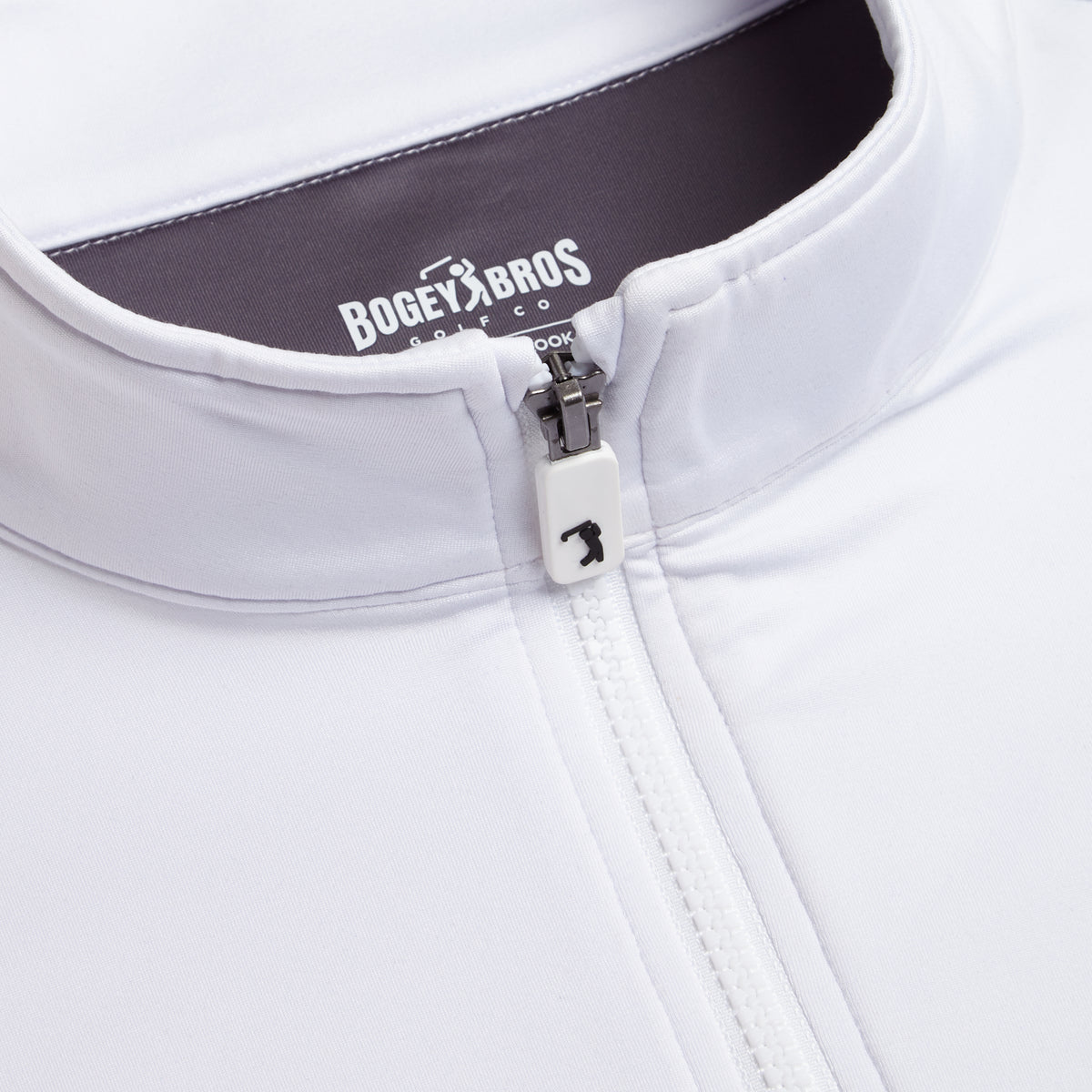 Close-up of the White - Q-Zip jacket, featuring a white zipper pulled halfway up with a small golfer icon on the zipper pull. The collar stands upright, and inside the collar, a gray tag displays the BOGEY BROS brand and logo in white with “GOLF CO.” below. Designed for both style and performance, the White - Q-Zip offers an athletic fit ideal for active days on or off the course.