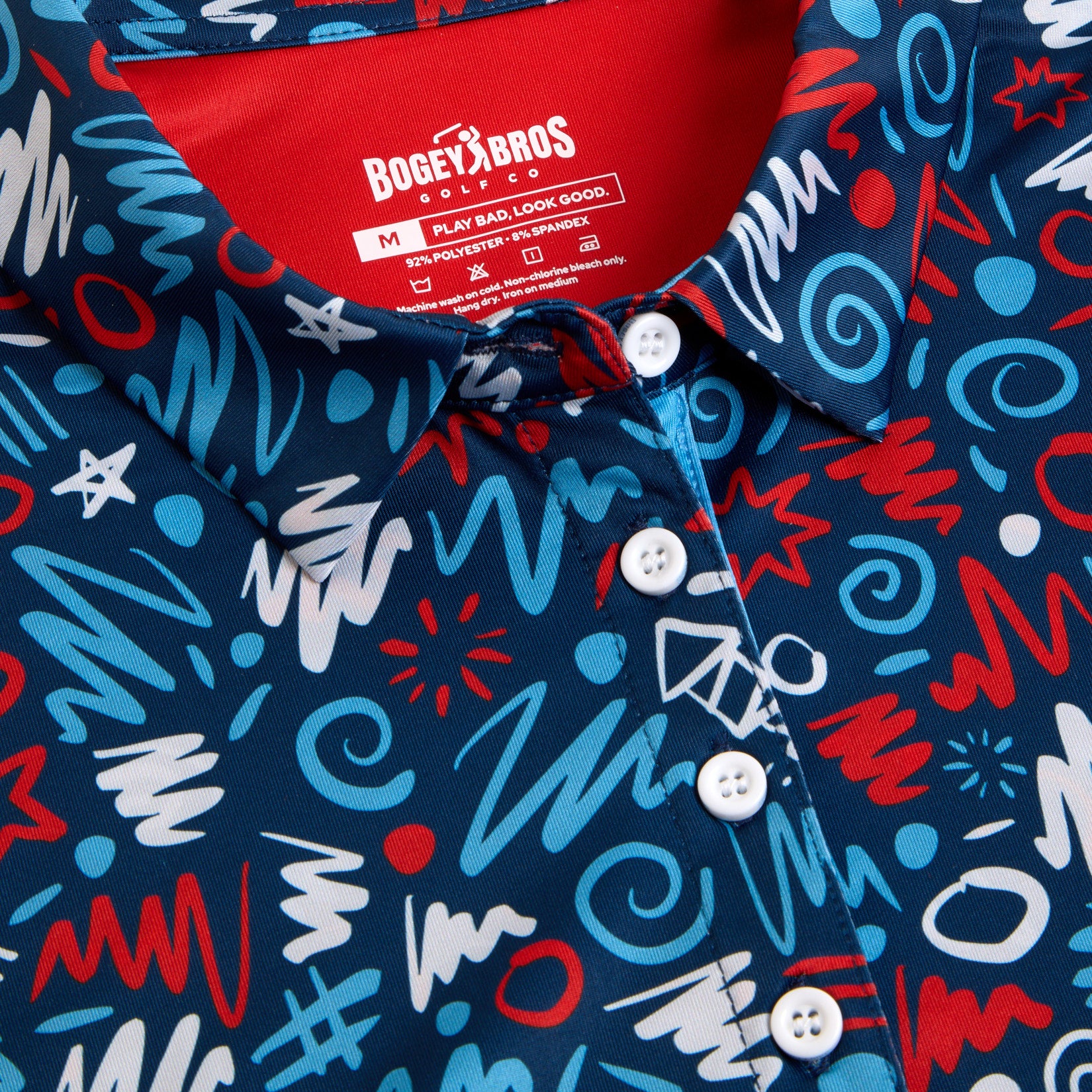 A close-up of a navy blue polo shirt with a chaotic, colorful abstract pattern of squiggles, stars, hashtags, and circles in red, light blue, and white. The shirt has a red collar and white buttons.