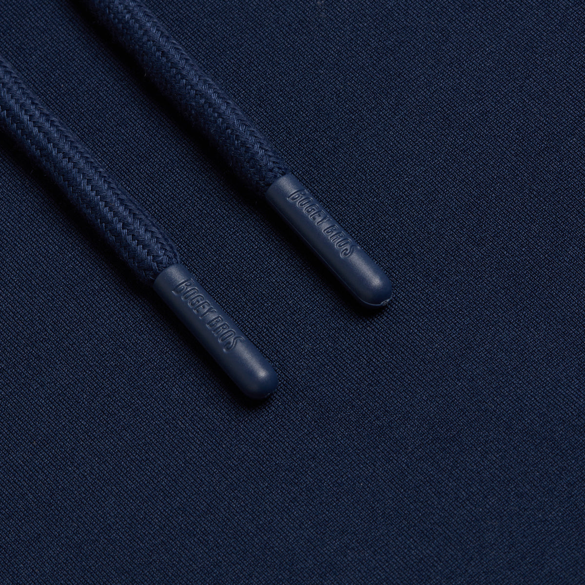 Close-up of two thick, braided navy blue drawstrings from the Navy - Hoodie, resting on matching fabric. The plastic aglets are embossed with “NICCE LONDON,” both clearly visible. The image highlights the detailed texture and craftsmanship of the materials, drawing attention to features inspired by athletic shorts, such as moisture-wicking properties for enhanced comfort.