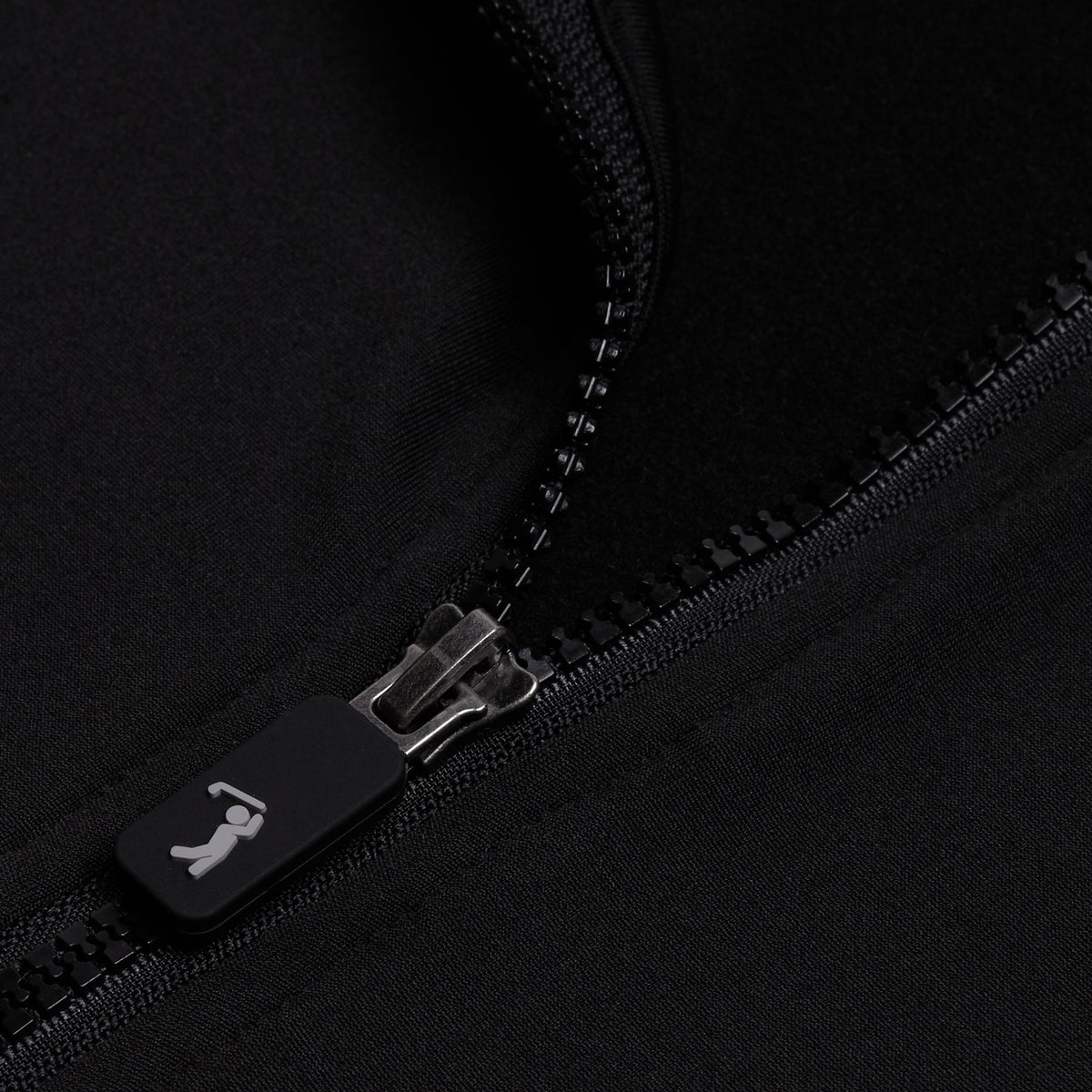Close-up of a partially open Black - Q-Zip on black fabric. The matte black zipper pull features a small white silhouette of a person swinging a golf club. The athletic-fit fabric has a smooth, slightly shiny texture.