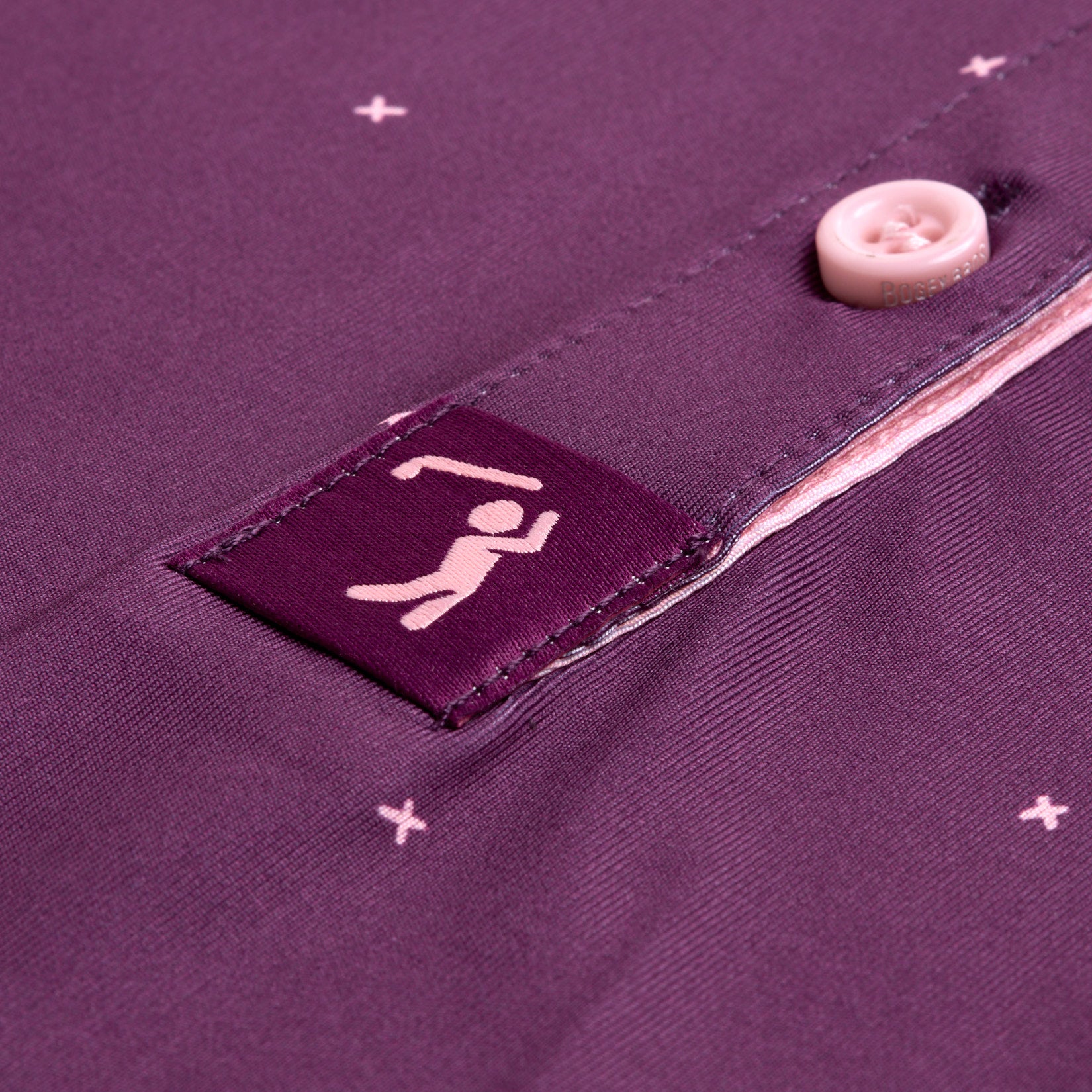 Close-up of the Exes - Plum - Women's Polo in an athletic fit, featuring light pink buttons, tiny white embroidered crosses, and a small square patch with a barbell lifter near the button placket.