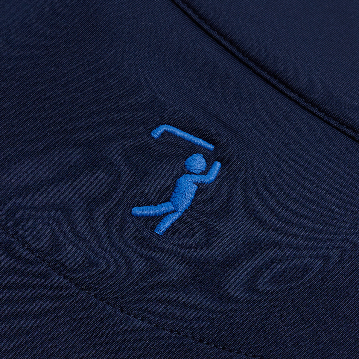 A close-up of the Navy - Q-Zip fabric highlights a small, light blue embroidered figure swinging a golf club. The stitching creates a stylized golfer in mid-swing with curved lines and simple shapes that stand out against the smooth, dark navy background. Designed for performance, the Navy - Q-Zip also features moisture-wicking technology to help keep you comfortable all day long.