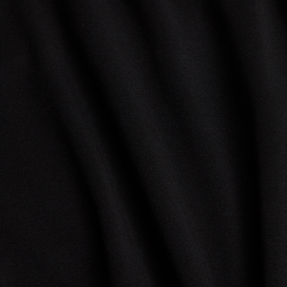 A close-up of black fabric with soft, diagonal folds. The surface appears smooth and matte, with gentle shadows created by the draping. Ideal for the Black - Hoodie, this material offers no visible patterns or textures other than the natural creases in the cloth.