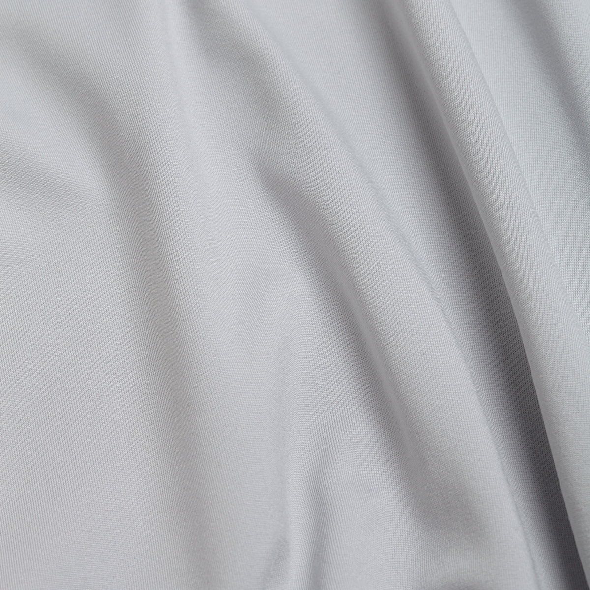 A close-up of smooth, light gray fabric with soft, flowing folds and gentle creases creates subtle shadows and highlights the texture across the surface—perfect for the Bone - Hoodie, featuring moisture-wicking properties to keep you comfortable during any activity.