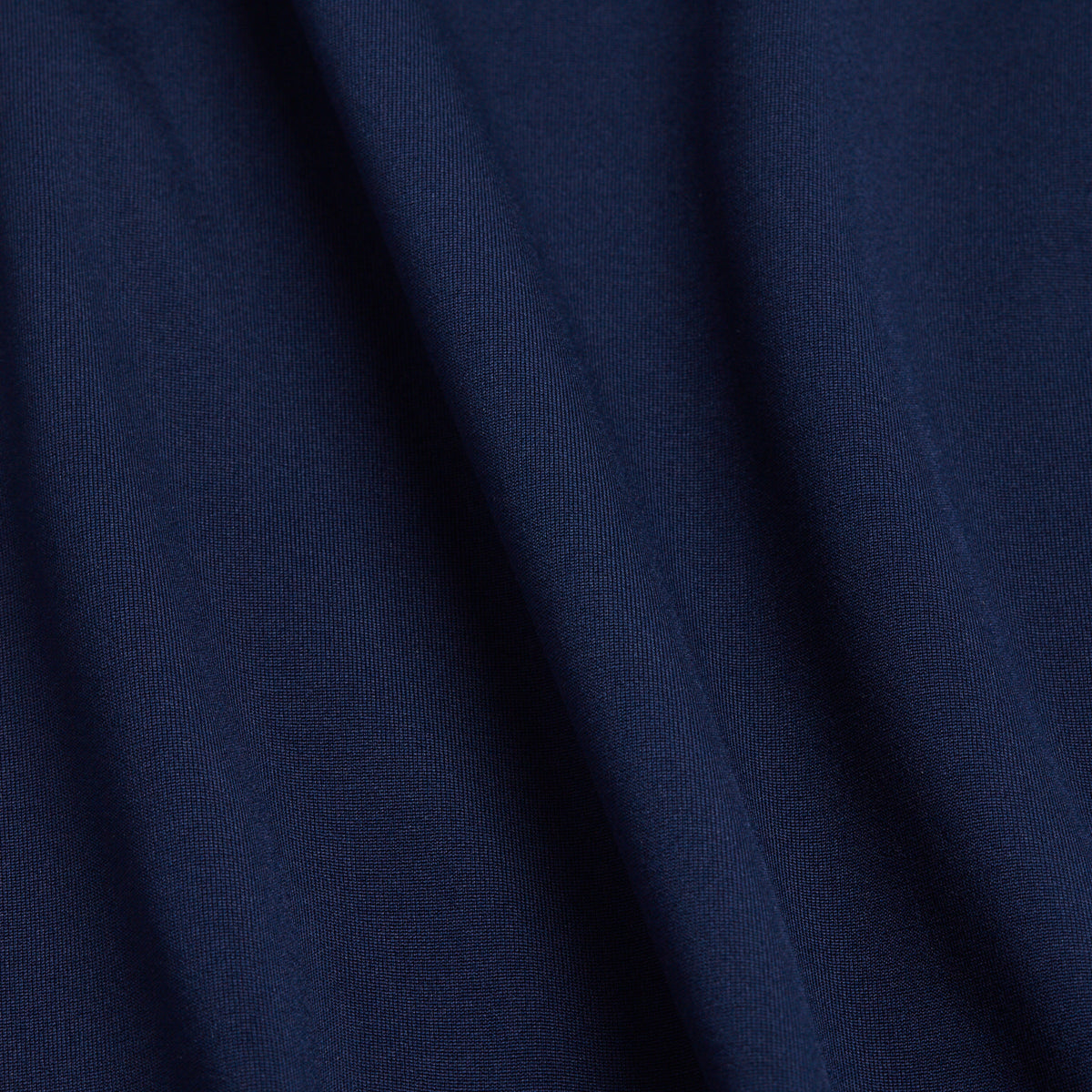 Deep navy blue fabric with a soft, smooth texture and gentle folds that create subtle shadows. The fine weave detail is apparent up close, adding depth and richness to the color. Crafted for hoodies, this material offers moisture-wicking properties and UPF 50 protection. It features a clean appearance with no visible patterns or embellishments.