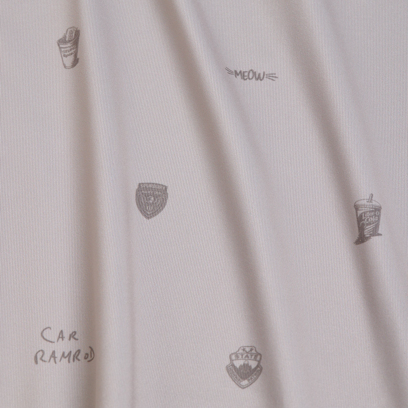 White fabric with small, sparse black line illustrations: two soda cups, three police badge shapes, the word MEOW, and the text CAR RAMROD, all randomly placed. The fabric shows subtle vertical folds and shadows throughout.