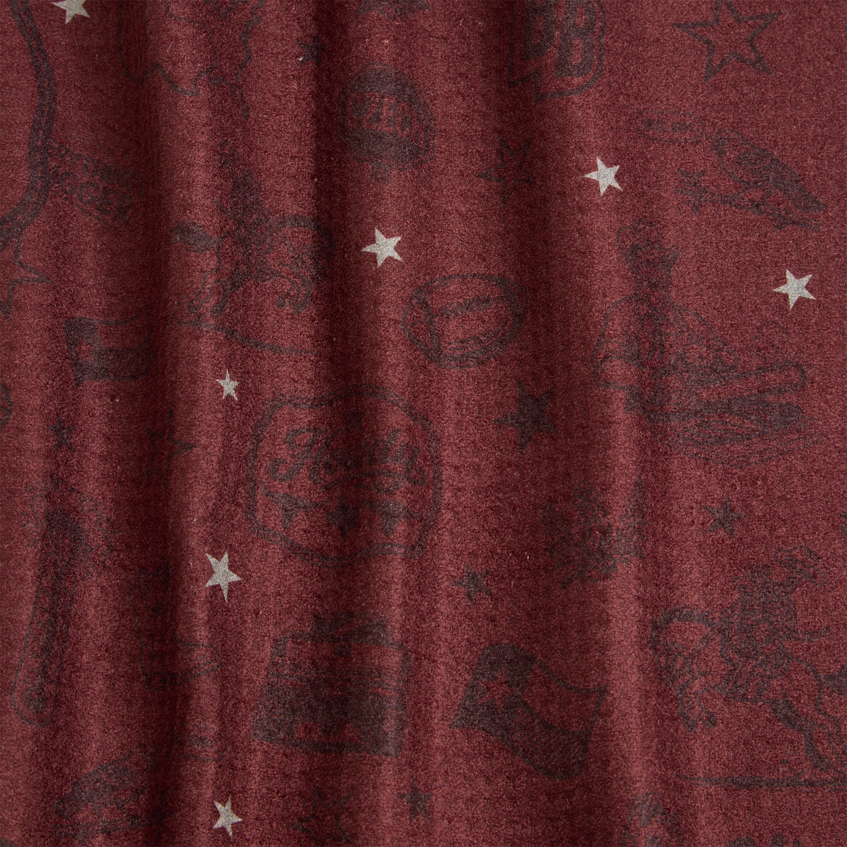 Burgundy fabric with dark, faintly visible cartoon illustrations and scattered white stars. The fabric appears to have gentle folds, giving it a slightly wavy texture. The patterns include various playful shapes and objects.