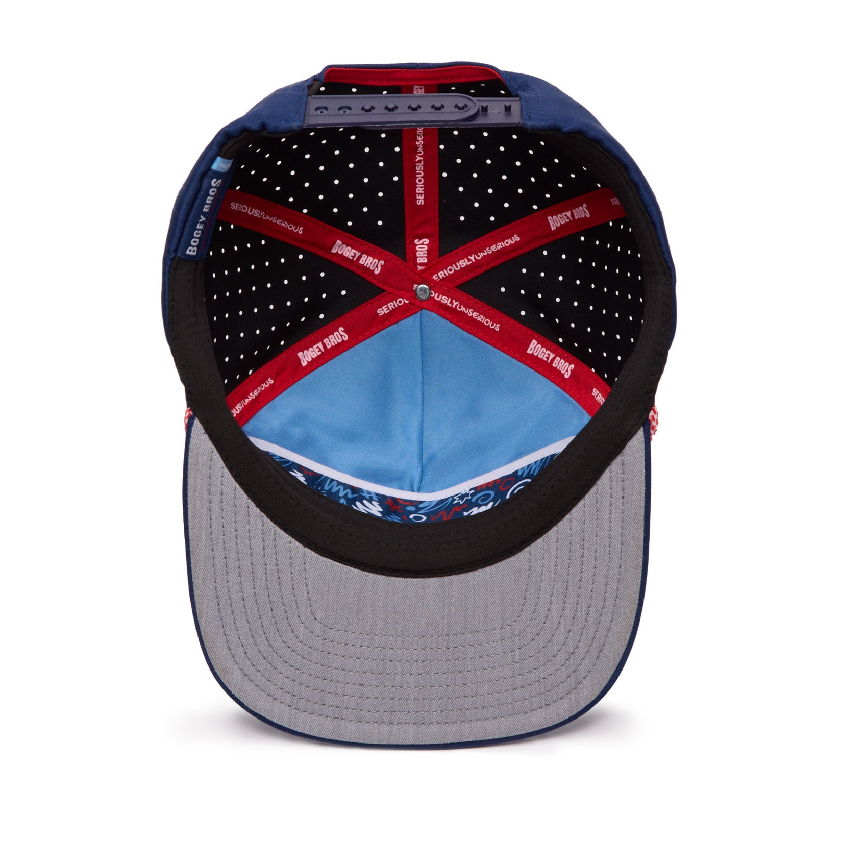 The image shows the inside view of a baseball cap. The cap’s interior lining includes red taped seams with white text, black fabric with white polka dots, and a blue section. The brim is gray on the underside with a patterned blue inner band.