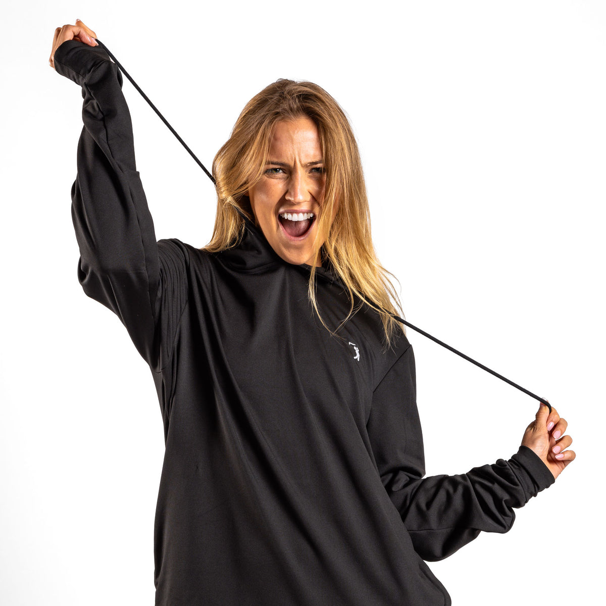 A woman with long blonde hair wears the Black - Hoodie, pairing it with athletic shorts as she smiles energetically and pulls on the hoodie’s drawstring against a plain white background.