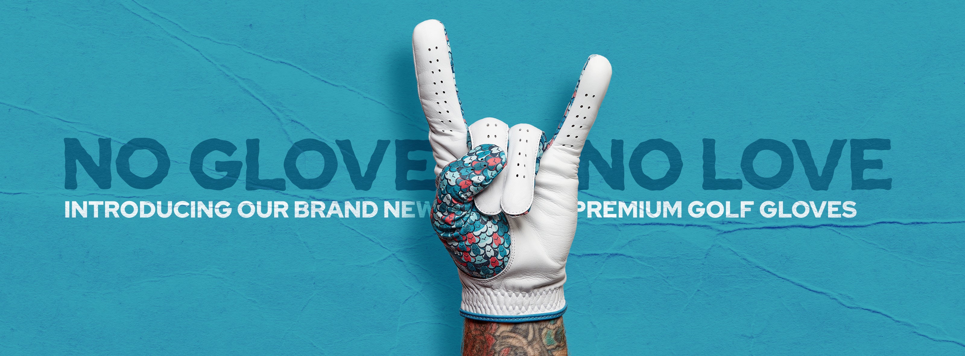 A tattooed hand wearing a white golf glove with a blue and red patterned index and pinky finger makes the rock on gesture against a blue background. Text reads: NO GLOVE NO LOVE. INTRODUCING OUR BRAND NEW PREMIUM GOLF GLOVES.