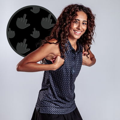 A smiling young woman with curly hair poses playfully, flexing her arms in a sleeveless top. Behind her is a black circle with gray hand icons making the middle finger gesture. She’s wearing the Birdie Finger - Raven - Women's Polo.
