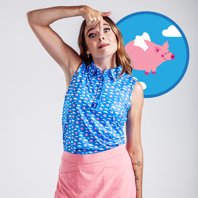 A woman in the "Pigs Fly - Women's Polo" with white and pink clouds makes a silly face, holding her nose and lifting her lip. Behind her, a cartoon flying pig with wings appears inside a blue circle.