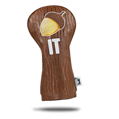 The Nut It - Driver Headcover is a brown, wood-textured PU leather cover featuring an embroidered acorn above white "IT" letters, plus a small white tag with a black logo. It’s shown on a white background with a subtle shadow.