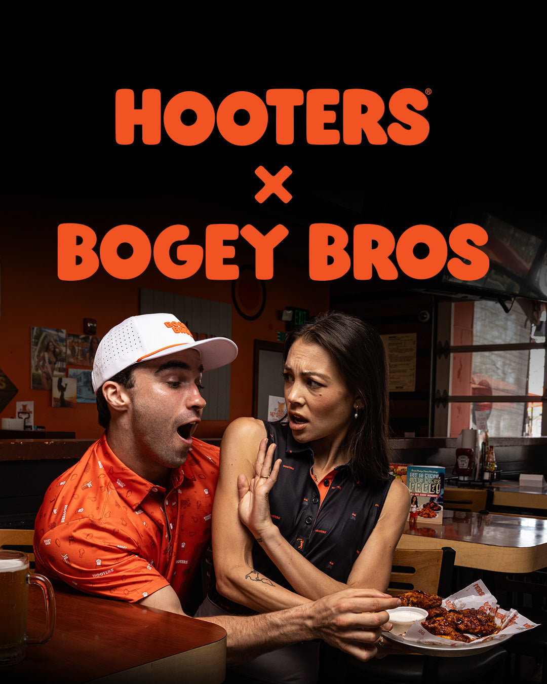 A man in a Hooters cap and shirt reacts with surprise as a woman next to him looks annoyed, pushing his arm away while holding a chicken wing; Hooters x Bogey Bros logo above them.