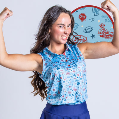 A woman flexes her arms and grins. She wears a blue patterned sleeveless shirt and blue skirt. The background is plain, with a circular inset highlighting the shirt’s light blue sports-themed pattern, featuring logos, stars, and graphics.