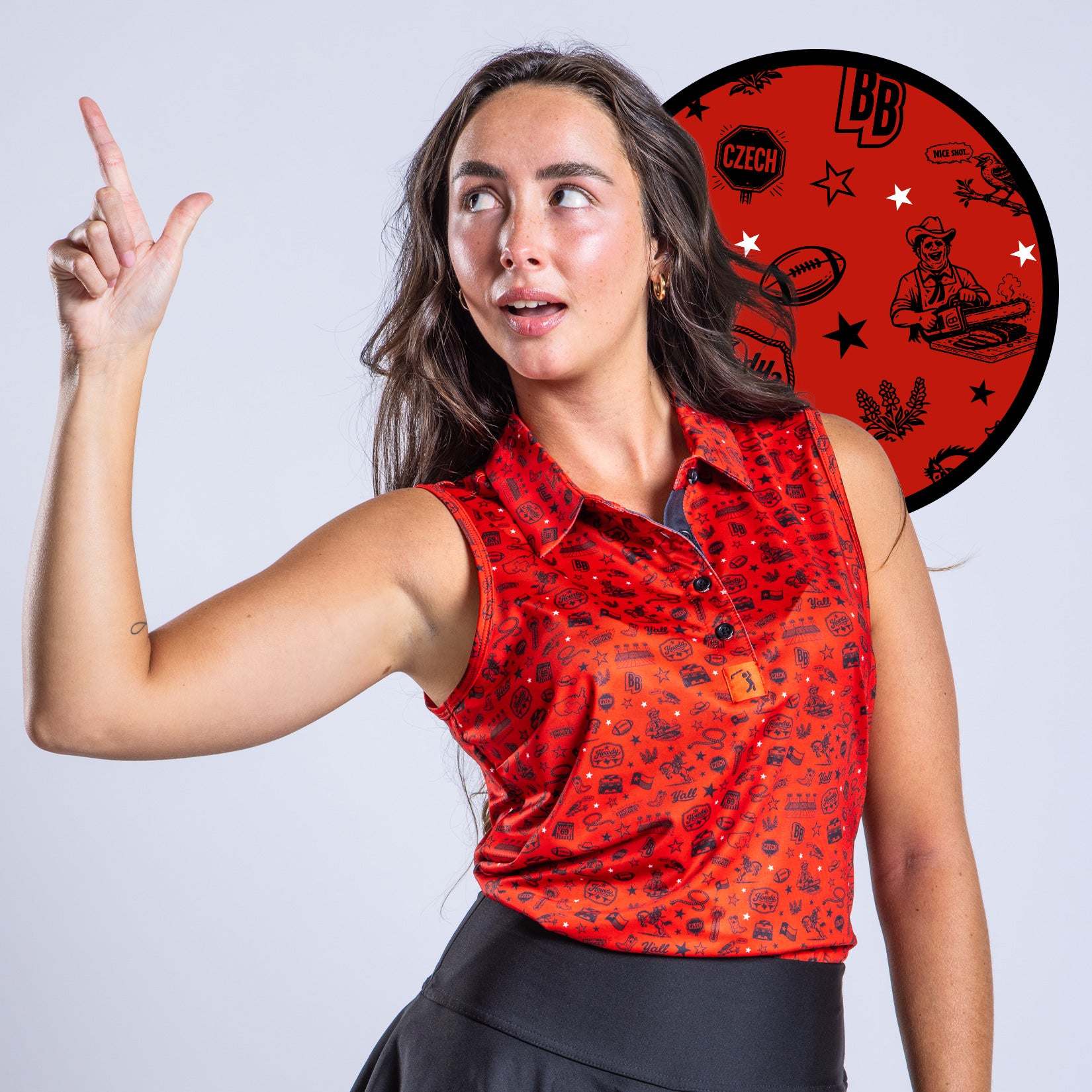 A woman with long brown hair wears a red, patterned sleeveless shirt and black skirt, posing with her left arm raised and finger pointed up. Behind her is a red circular disc with black and white illustrations and logos. She looks off to the left, smiling slightly.