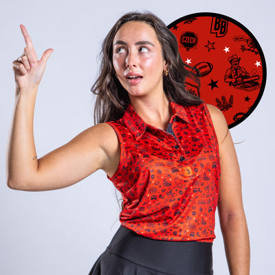 A woman with long brown hair wears a red, patterned sleeveless shirt and black skirt, posing with her left arm raised and finger pointed up. Behind her is a red circular disc with black and white illustrations and logos. She looks off to the left, smiling slightly.