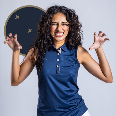 A woman with curly hair smiles brightly, wearing the Exes - Navy - Women's Polo, a sleeveless athletic-fit shirt with white dots. She poses playfully with raised hands against a plain background featuring a dark circle and two light X marks.