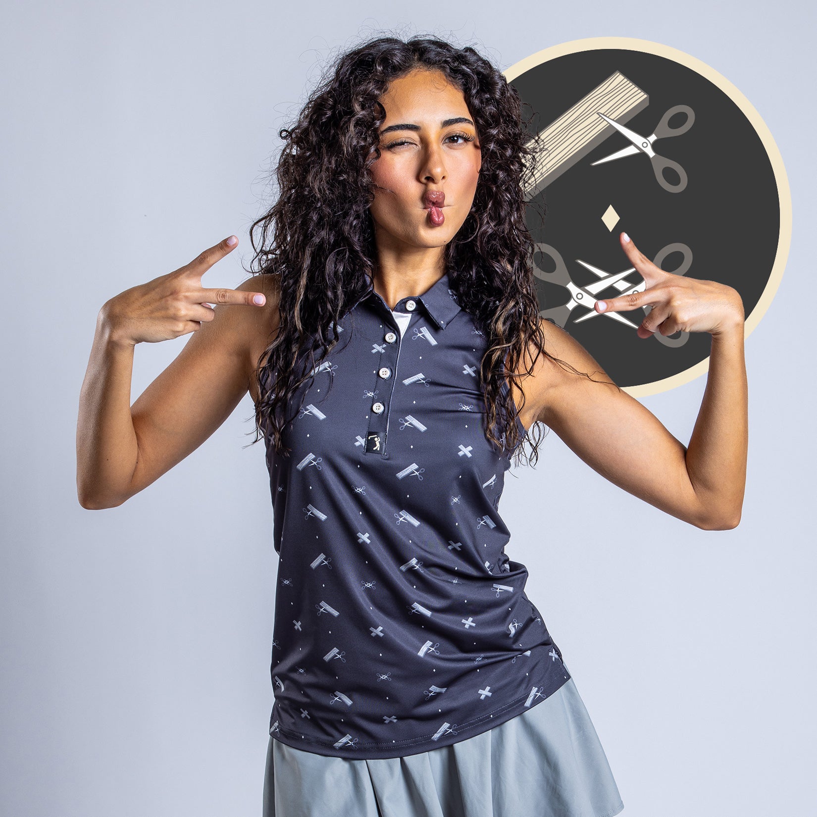 A curly-haired woman in a sleeveless, moisture-wicking navy Scissor Me Timbers - Women's Polo and light gray skirt makes playful peace signs. Behind her is a circular graphic featuring scissors, a ruler, and pencil on a dark background.