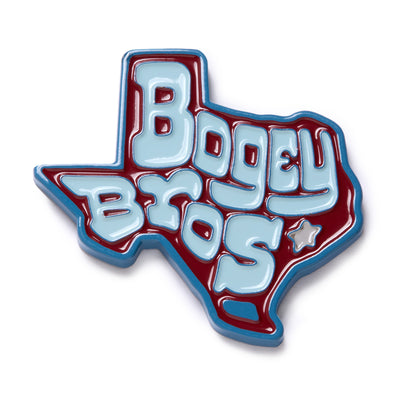 A pin shaped like Texas with “Bogey Bros” in bold, light blue letters outlined in white and blue on a maroon background. A small star appears near the bottom right. The edges are also outlined in blue.