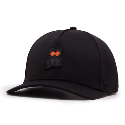 The Night Owl Performance Golf Hat is a black snapback with a curved brim, perforated side panels, and a raised black owl patch with vivid orange eyes. Made from performance material, it features a subtle black logo tag by the brim.