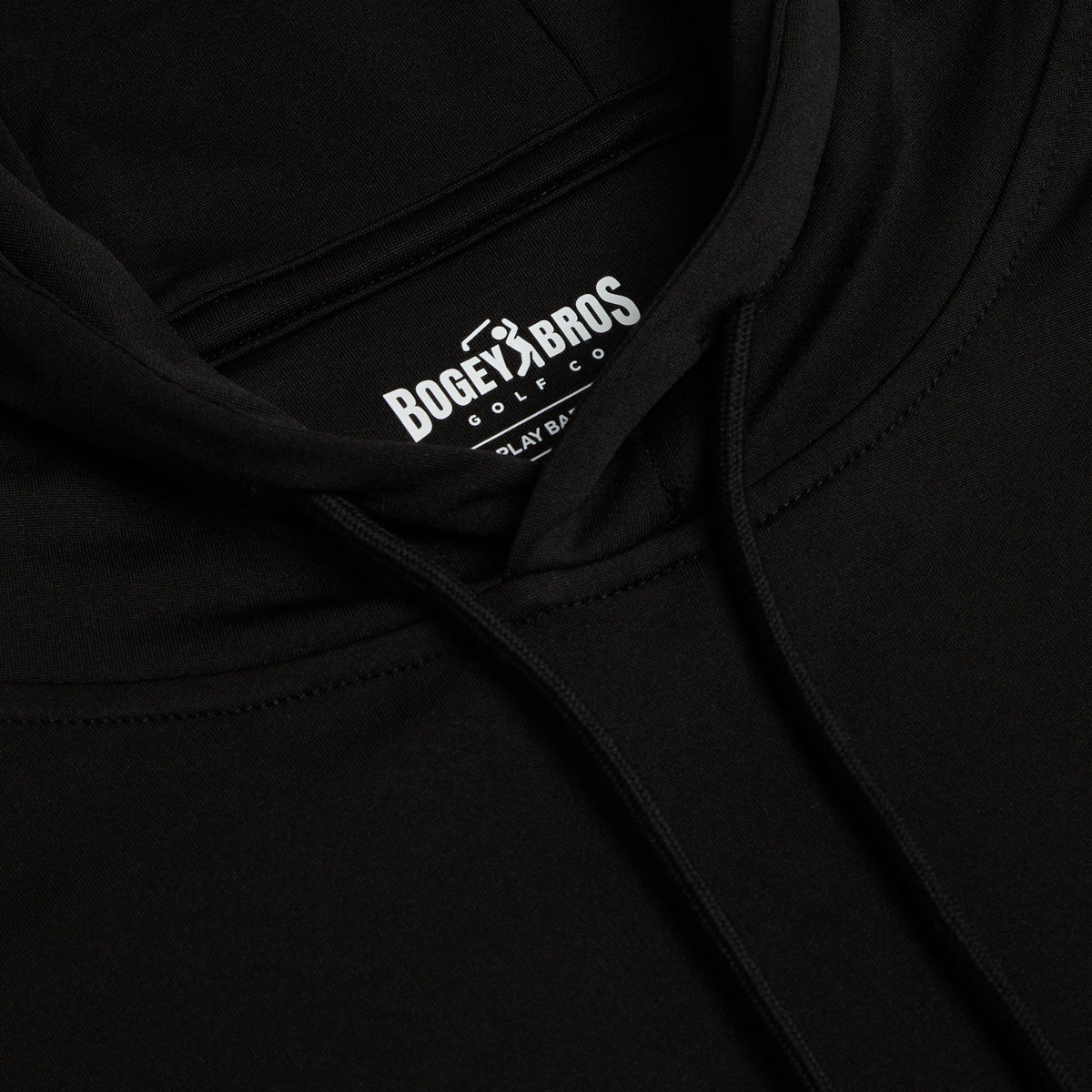 Close-up of the Black - Hoodie highlighting a white Bogey Bros Golf Co logo on the inside neck label, with visible drawstring and seam details against the fabric. The image focuses on the brand label and showcases the hoodie’s smooth, moisture-wicking texture.