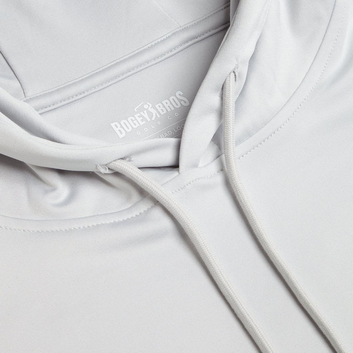 Close-up of the Bone - Hoodie in light gray, featuring a hood with drawstrings. The inside neckline displays the BOGEY BROS GOLF CO. logo in white with additional smaller text underneath. Made from soft, smooth fabric with visible seam stitching, this hoodie offers moisture-wicking properties to keep you comfortable during your game.