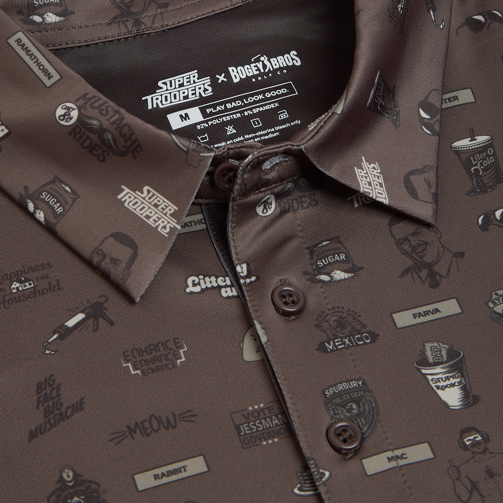 Close-up of a brown button-up shirt with various beige and cream Super Troopers-themed illustrations, including faces, text, mustaches, coffee cups, badges, and random words. The shirt tag at the collar displays branding from Super Troopers and Bogey Boys.