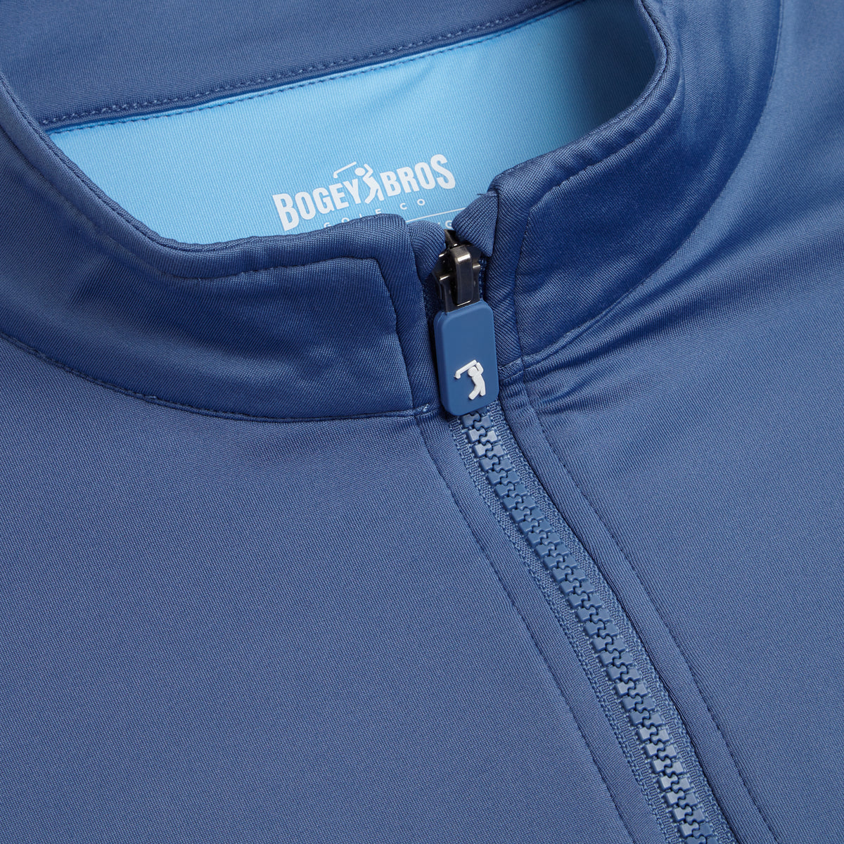 Close-up of the Cooler Blue - Q-Zip’s zipper and collar, featuring BOGEY BROS and a golfer logo printed inside the collar on a light blue background. The zipper pull displays a small golfer icon as well. Crafted from super stretchy, smooth, and lightweight fabric, this jacket provides an athletic fit designed for active comfort.