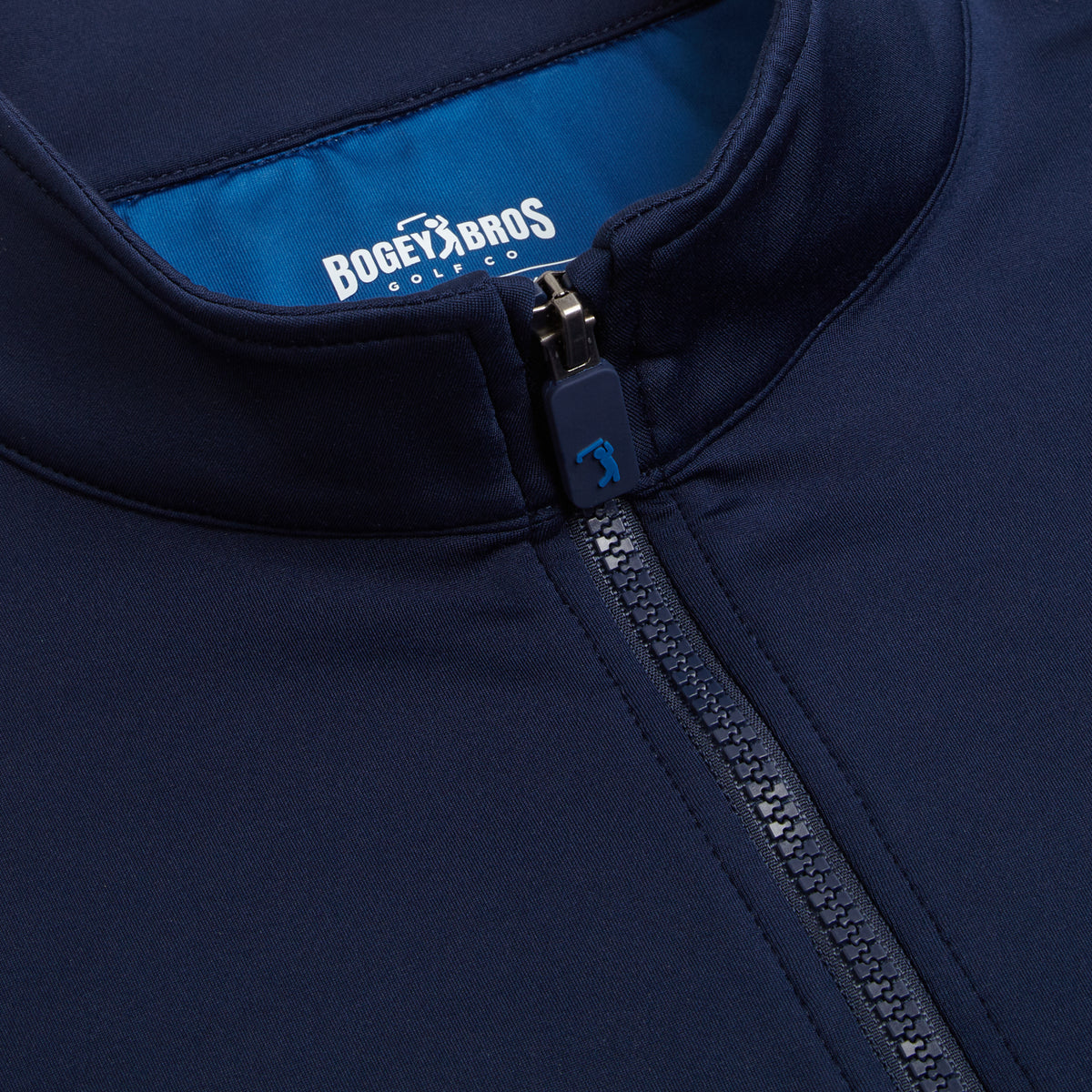 Close-up of the Navy - Q-Zip jacket, featuring a zippered front, small stand-up collar, and athletic fit. The zipper pull includes a golf club icon, while the bright blue inside lining displays “BOGEY BRO$ GOLF CO” printed in white on the inside of the collar. Designed for comfort and performance, this jacket offers moisture-wicking technology to help keep you dry during every round.