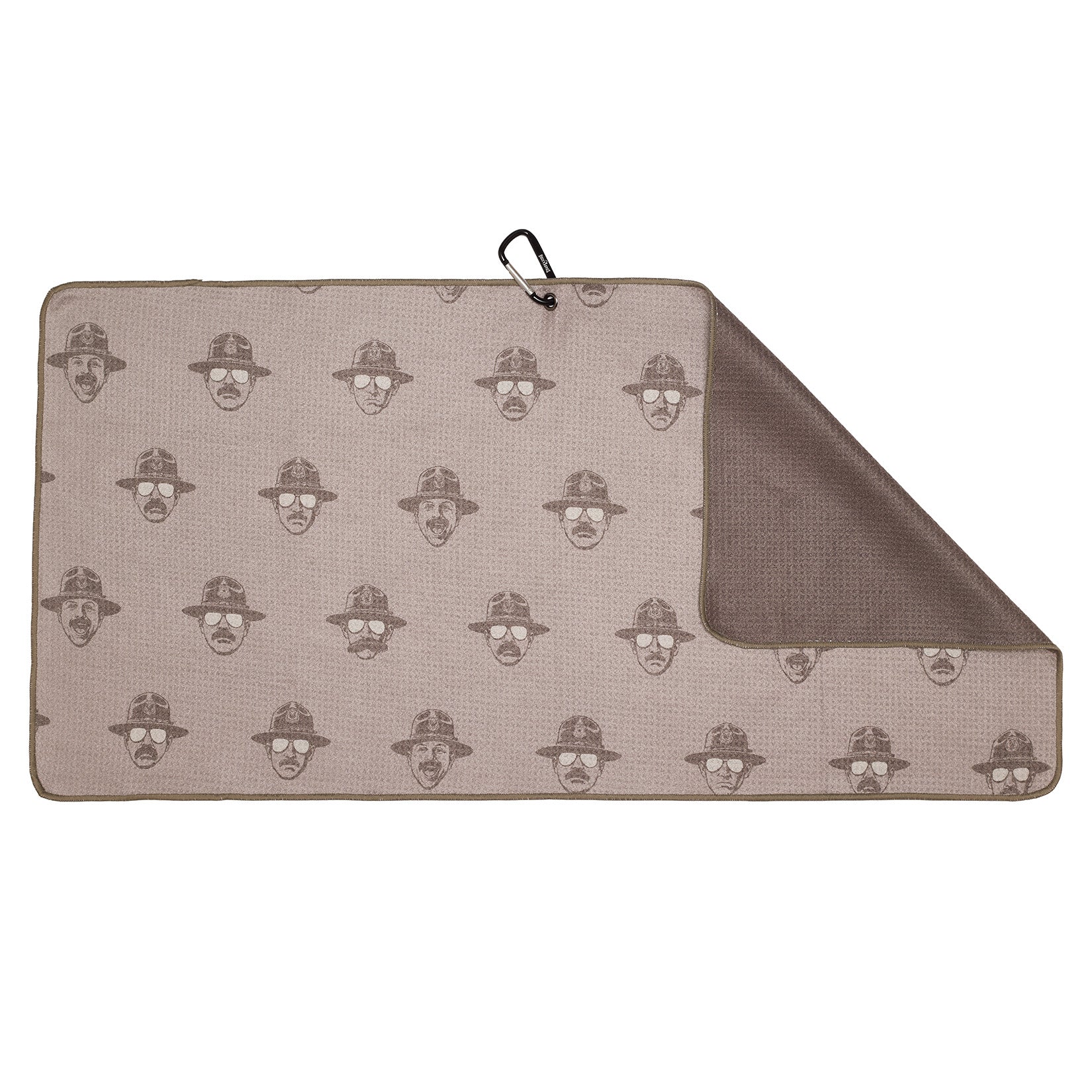 A rectangular beige mat with repeated patterns of a face wearing glasses and a hat. One corner is folded, revealing a textured brown underside. A black clip is attached to the mats upper left corner.