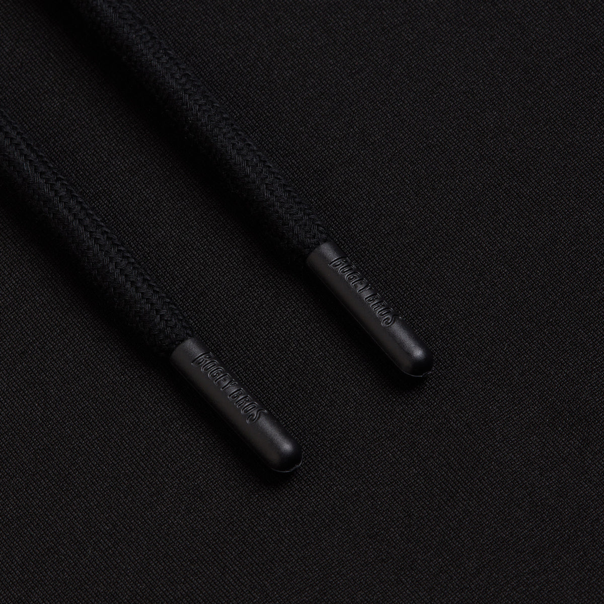 Two drawstrings from the Black - Hoodie, each capped with cylindrical, shiny metal aglets engraved with DIME MTL 2005, rest on a smooth black fabric surface. The durable finishes of both the braided strings and the hoodie’s premium material are clearly visible, reminiscent of high-quality athletic apparel.