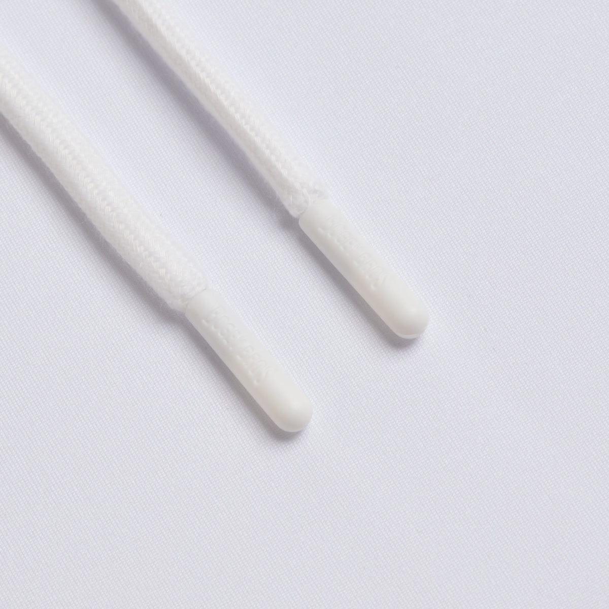 Close-up of two white shoelace tips, known as aglets, lying parallel on the smooth mesh fabric of the White - Hoodie. The cylindrical plastic aglets have a subtle texture visible on the laces, while soft and even lighting highlights the athletic fit and moisture-wicking qualities of the White - Hoodie’s fabric beneath them.