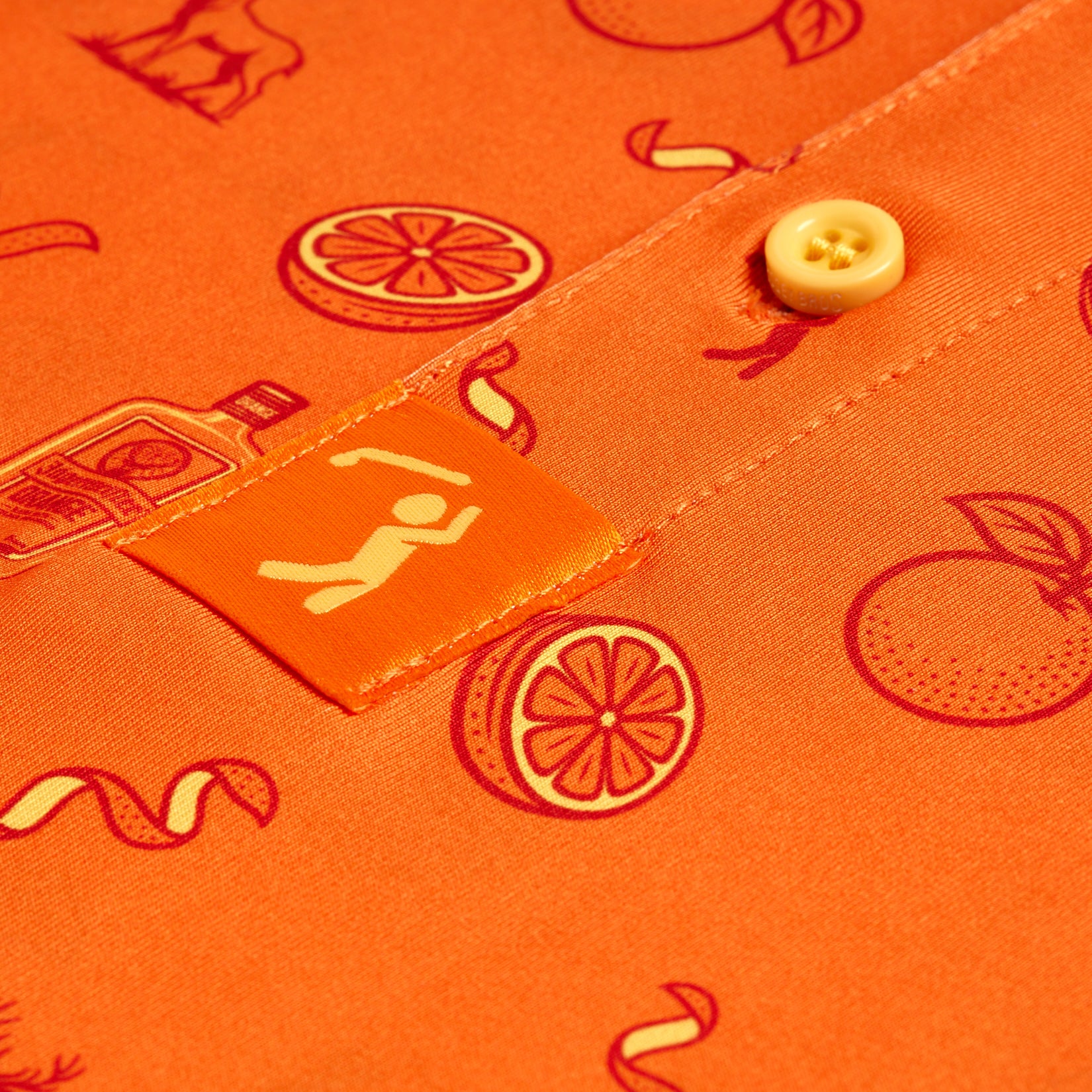 The Main Squeeze - Polo is an orange athletic-fit shirt with red line art of oranges, slices, a bottle, ribbons, and a person icon. It features a yellow button, fabric tag, and UPF 50 protection for sunny days.