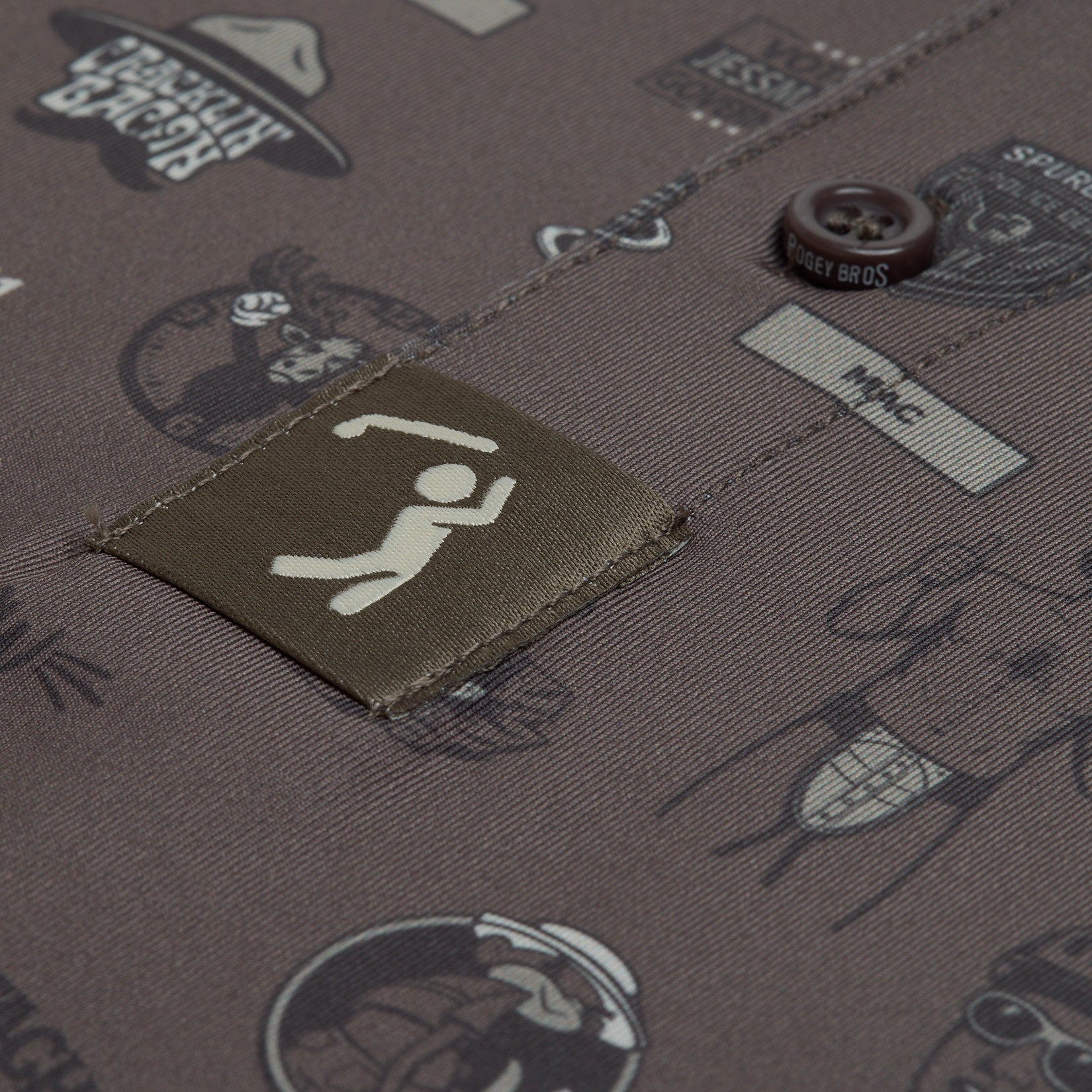 A close-up of brown fabric with a patch showing a white, stylized figure with raised arms. The fabric features various black-illustrated graphics and texts, including animal faces, hats, and button details. A round button labeled BRODY BROS is visible.