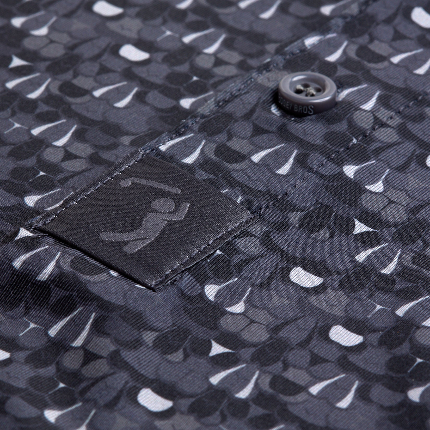 Close-up of the T&A - Fitty Shades - Polo, showing overlapping teardrop shapes, a button with stitched buttonhole, and a black label with a minimalist cricket figure. The satin-like fabric offers moisture wicking for comfort.