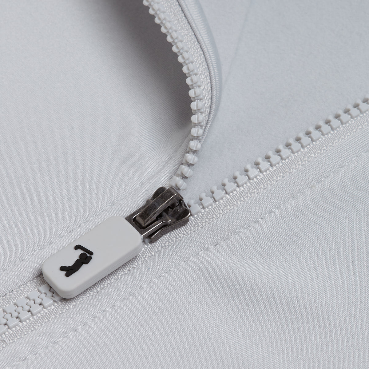 Close-up of the Bone - Q-Zip, featuring a white plastic zipper on light gray, athletic-fit fabric. The zipper slider displays a small shirt icon, while the visible zipper teeth and the smooth, slightly reflective moisture-wicking material convey a sleek look.