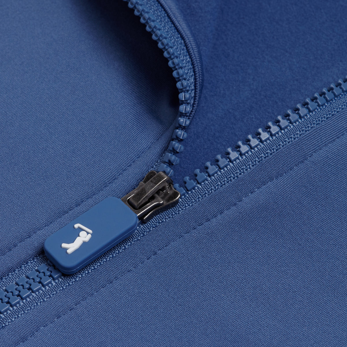 Close-up of the Cooler Blue - Q-Zip, featuring a blue zipper on moisture-wicking, super stretchy fabric. The partially open zipper reveals detailed stitching and teeth, while the pull tab displays a small white icon of a person lying down.