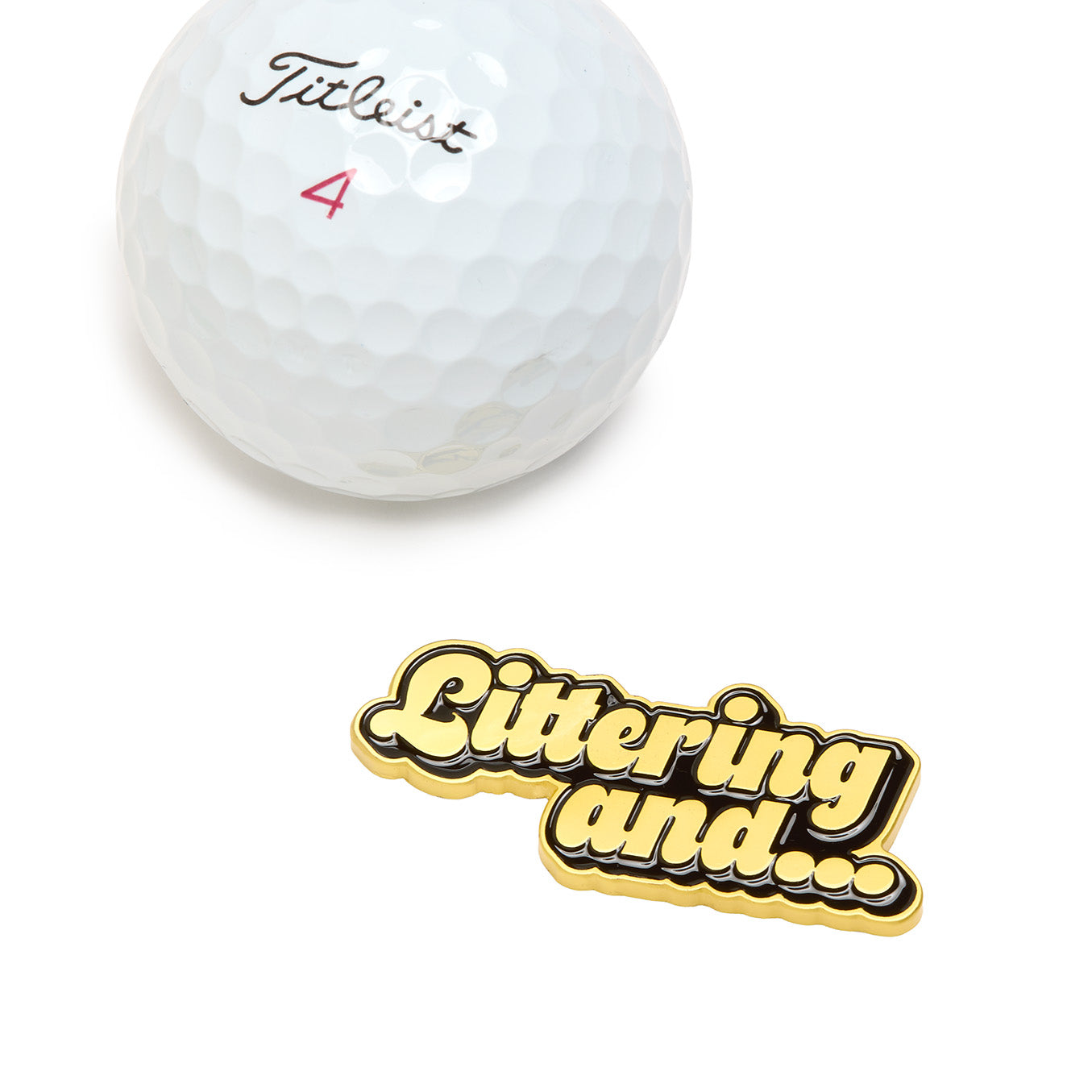 The Littering and... - Ball Marker, featuring a gold and black enamel finish with the words “Littering and...” in bold, bubble-style letters, is displayed on a plain white background above a white Titleist golf ball marked with a red number 4. This heavy metal marker is crafted with iron nickel plating for durability and comes equipped with a magnetic clip for convenient attachment to your golf gear.