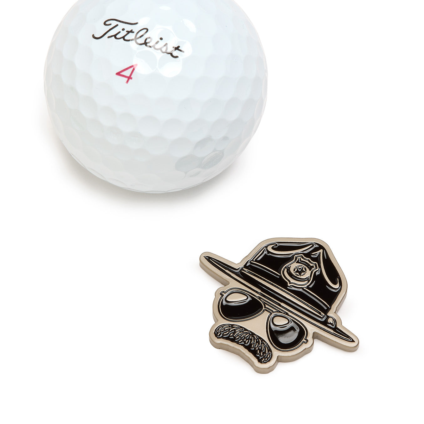 A white Titleist golf ball with a pink number 4 sits next to the Super Cop - Ball Marker, a black-and-gold pin shaped like a stylized face wearing sunglasses, a mustache, and a police hat with a badge. This accessory also doubles as a metal ball marker featuring iron nickel plating.