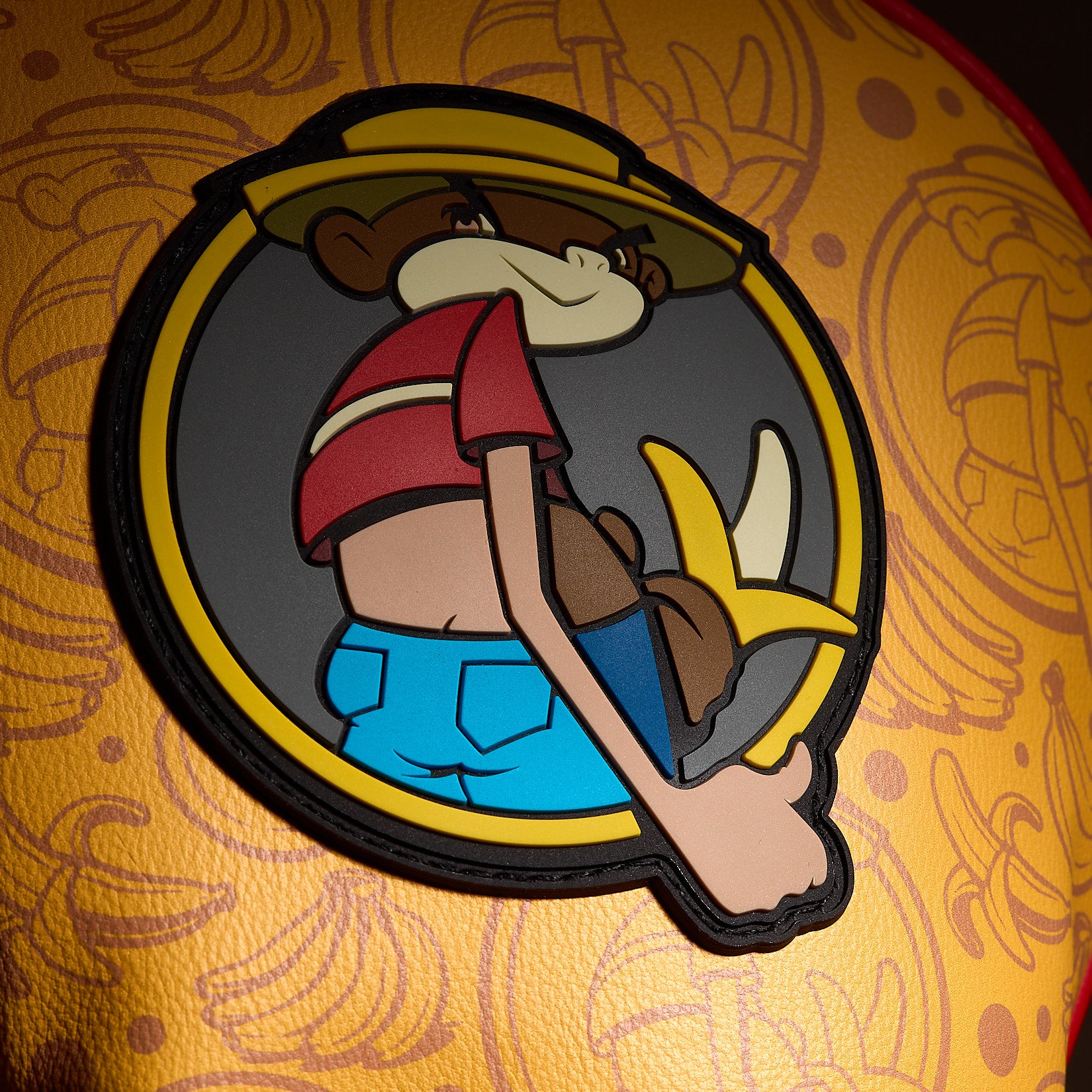 Introducing the Johnny Chimpo - Driver Headcover: This vibrant headcover features an embroidered cartoon patch of a playful monkey sporting a yellow hat, red striped shirt, and blue pants while holding a banana. Sewn onto high-quality PU leather with orange fabric adorned with banana and monkey face patterns, it’s outlined in black and set against a cheerful yellow background. Add this eye-catching woven label golf accessory to your collection for the perfect premium driver head cover with character!.